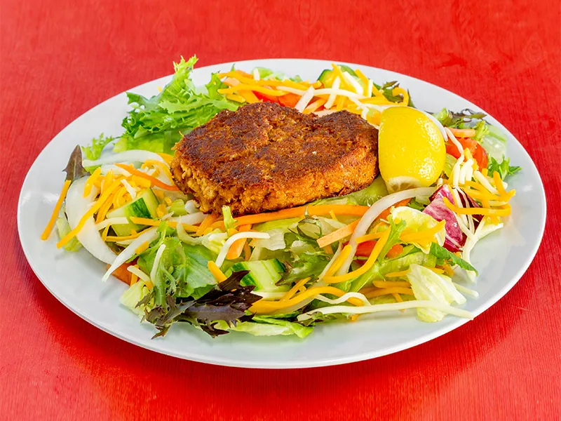Fresh salad topped with a golden-brown crab cake at This is Seafood, a Seafood Restaurant in District Heights